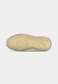 Talpa din cauciuc pentru pantofi sport cu textură circulară și modelată, predominant bej cu o nuanță ușoară. Prezintă un logo în apropierea zonei călcâiului.