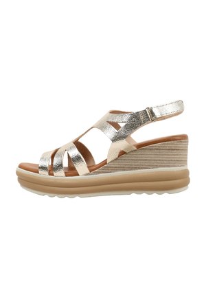 Sandalia de cuña para mujer en dorado metálico con tira ajustable en el tobillo y suela de plataforma acolchada en color beige.
