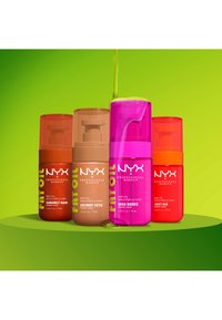 Four colorful NYX Professional Makeup body oil bottles labeled Caramelt Mami, Coconut Cutie, Suga Baddie, and Juicy Boo on a green surface.
