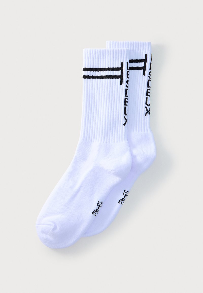 Paire de chaussettes blanches côtelées avec des rayures noires et un texte noir vertical sur le côté, présentées à plat sur un fond clair.