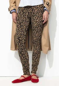 Leggings à motif léopard en tan et noir, associés à des ballerines rouges. L'ensemble est complété par un trench-coat beige et un haut gris.