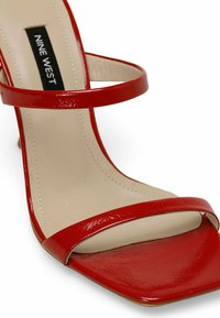 Red strappy high-heel sandal with a glossy finish, square toe, and contrasting beige insole. Brand label visible on the inner strap.