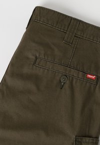 Πίσω μέρος ελιάς πρασινωπού παντελονιού Levi's με τσεπάκι με κουμπιά και κόκκινη ετικέτα με το λογότυπο Levi's στην άκρη της τσέπης.