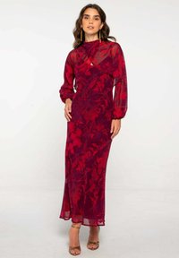 Robe longue rouge avec un motif floral, manches transparentes, col haut et silhouette fluide. Présente une texture lisse et un léger éclat.