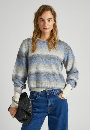 Jersey de punto con rayas horizontales en tonos de azul, gris y crema. Puños acanalados, cuello redondo, combinado con jeans azules y un bolso negro.