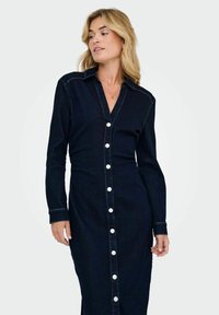 Robe en denim bleu marine avec des manches longues, fermeture à boutons sur le devant et col. Présente une taille ajustée et une jupe longue droite. Détail de couture classique.
