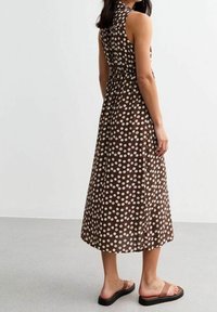 Ruskea pilkullinen midi-mekko, jossa on korkea kaula-aukko ja selkäside, valmistettu kevyestä kankaasta, yhdistettynä tasapohjaisiin sandaaleihin.