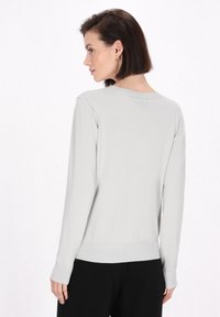 Hellgrauer langärmeliger Pullover mit rundem Ausschnitt, gerippten Bündchen und Saum. Die Textur erscheint glatt und leicht dehnbar.