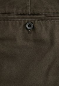 Tissu vert olive foncé avec une texture lisse, présentant un bouton noir en haut avec le texte "DENIM SUPPLY CO." au-dessus d'une couture.