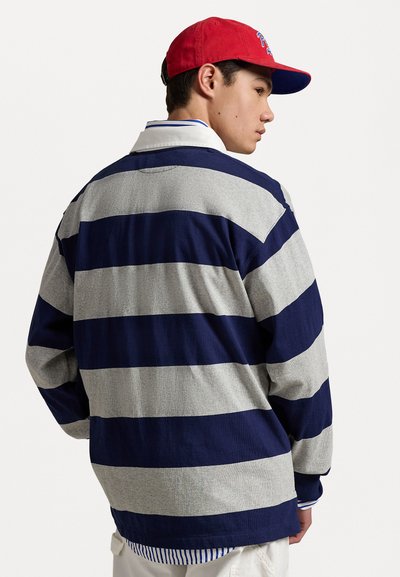 Long-sleeve striped shirt in navy and grey cotton. Features a collar and a hem with a blue and white striped accent. Red cap worn.