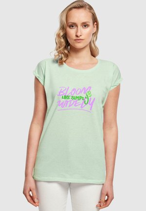 Mintgrünes T-Shirt mit kurzen Ärmeln und aufgerollten Bündchen, das mit einem grafischen Druck in Pink und Grün versehen ist, auf dem steht "BLOOM LIVE SIMPLY WIDELY."