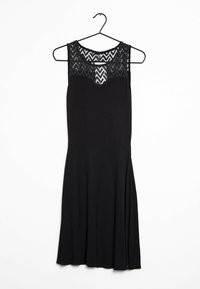Schwarzes Kleid mit tailliertem Oberteil und ausgestellt schmeichelndem Rock. Verfügt über einen strukturierten Spitzenoberteil mit Zickzackmustern. Hängt an einem schwarzen Kleiderbügel.