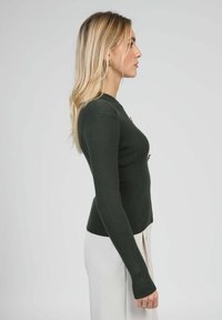 Haut vert foncé côtelé à manches longues avec une coupe ajustée. Il présente un col rond et des boutons décoratifs sur les côtés. Texture lisse et silhouette slim.