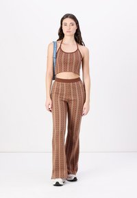 Barna mintás crop top, amelyhez illeszkedő, laza szárajú nadrág tartozik, függőleges csíkokkal és virágos részletekkel. A modellen fehér sportcipő van.