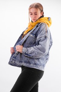Denim jacket in light blue with a relaxed fit, featuring silver buttons and seams. Paired with a thick, mustard yellow knitted scarf.