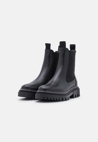 Bottines Chelsea en cuir noir avec des panneaux latéraux élastiques, semelle noire robuste et détail de surpiqûre blanche contrastante. Talon plat, hauteur cheville.