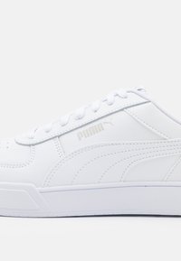 Weiße Sportschuhe aus glattem Leder. Mit einer flachen weißen Sohle, rundem Zehenbereich und dezenten silbernen Logodetails an der Seite.