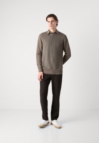 Suéter de punto acanalado marrón con cuello tipo polo, combinado con pantalones oscuros y zapatillas blancas. Textura suave, diseño ajustado.