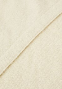 Tissu tricoté de couleur crème douce avec une texture visible et un bord plié en diagonale à travers le cadre.