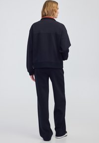 Sudadera azul marino con un cuello alto, puños y dobladillo acanalados. Combinada con pantalones de pierna ancha a juego y zapatos blancos. Textura de tela suave.