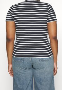 Person iført en marineblå og hvid vandretstribet kortærmet skjorte og lyseblå denimjeans set bagfra.