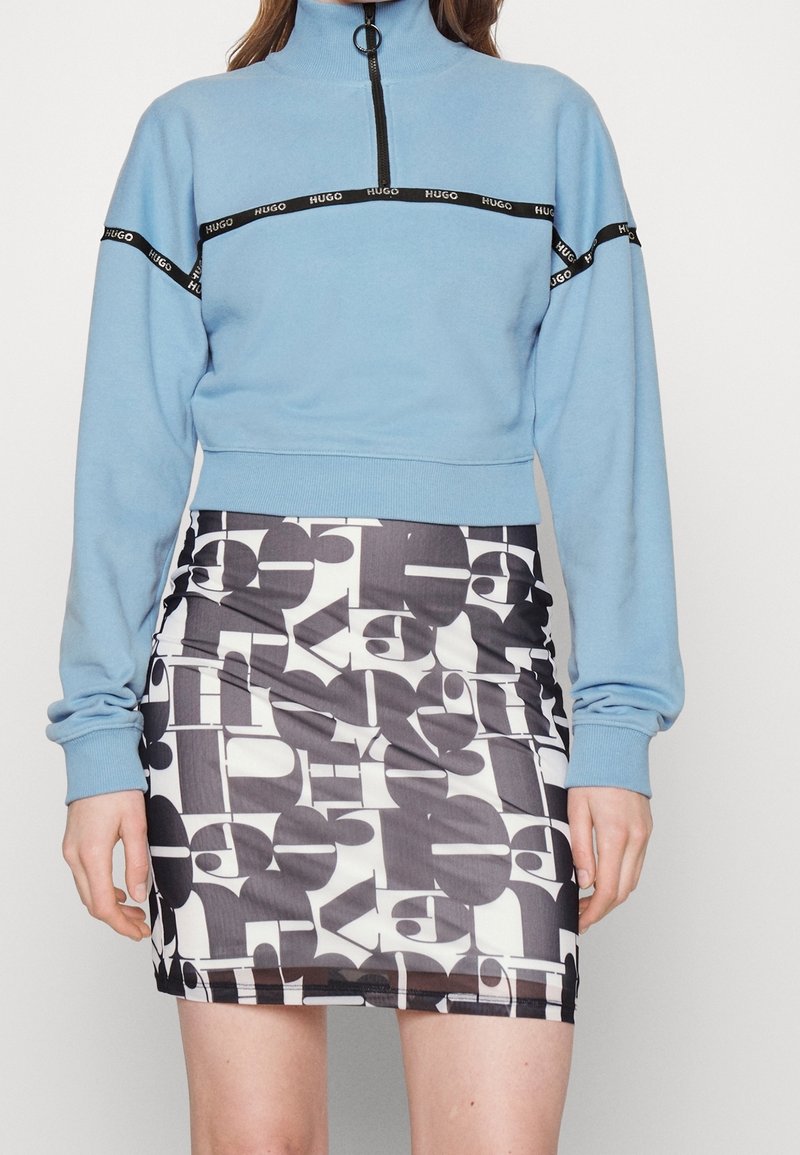 Lichtblauwe cropped sweatshirt met een hoge kraag en zwarte rits. In combinatie met een zwart-witte minirok met een patroon van gestileerde letters.