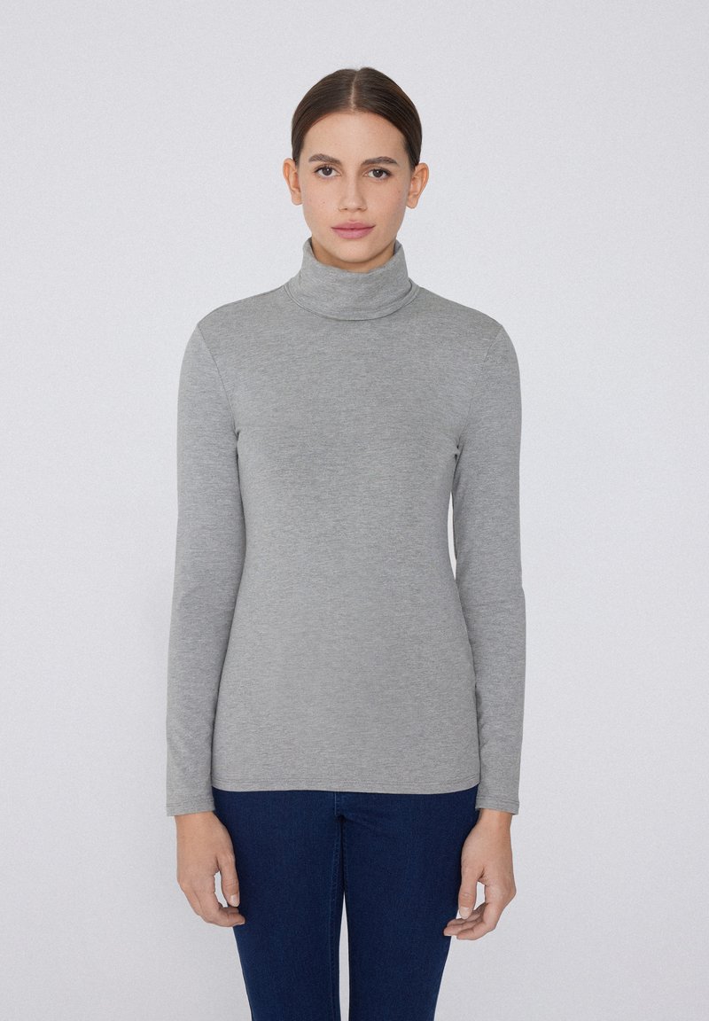 Maglione a collo alto grigio chiaro in tessuto morbido con maniche lunghe, design aderente e cuciture minime, abbinato a jeans blu scuro.