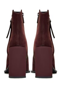 Stivaletti ankle in suede bordeaux con tacco quadrato, dotati di zip laterale e dettaglio di cucitura verticale sul retro.