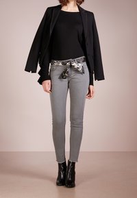 Černý blejzr přes přiléhavý černý svetr, doplněný šedými skinny džínami a vzorovým opaskem. Černé kotníkové boty dokončují celkový vzhled.