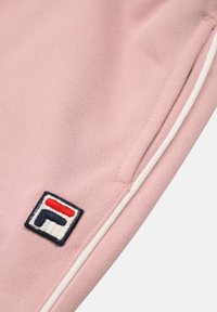 Rosa tyg med en mjuk textur, prytt med ett vitt accentband och en Fila-logotyp med röda, vita och blå inslag.