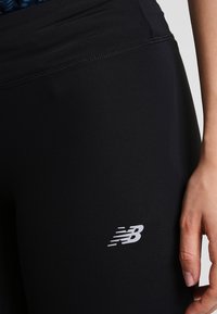 Leggings neri realizzati in tessuto elasticizzato, con vita alta e un piccolo logo argento sul lato sinistro. Texture liscia senza motivi.