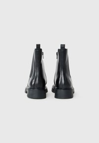 Bottines en cuir noires avec une texture lisse, dotées d'une semelle à plateforme basse et de fermetures éclair à l'arrière.