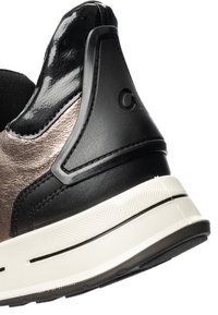 Primer plano del talón de una zapatilla negra y metálica con suela blanca texturizada y logotipo en relieve en el contrafuerte negro del talón.