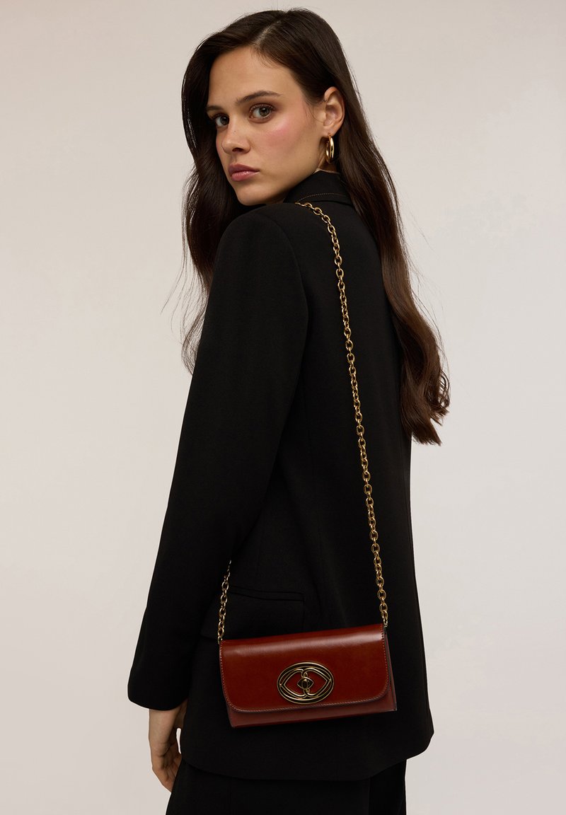 Borsa a spalla in pelle marrone con tracolla in catena dorata, dotata di una chiusura ovale decorativa. Struttura liscia, forma rettangolare e design minimalista.