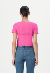 T-shirt attillata rosa corta con scollatura rotonda, maniche corte e un tessuto trasparente, abbinata a jeans in denim blu a vita alta.