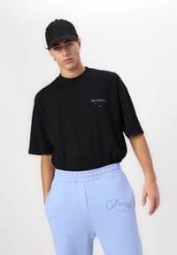 Black short-sleeve t-shirt with logo, paired with light blue sweatpants featuring embroidered text and an elastic waistband.