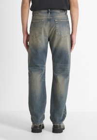 Jeans de mezclilla azul con un lavado desgastado, diseño de pierna recta, cinco bolsillos y costuras visibles. Llevados con calzado negro.