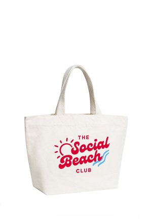 White canvas tote bag with short handles and red text "The Social Beach Club" with a sun and blue wave design on front.