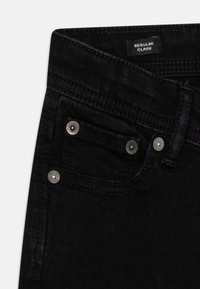 Svarta denimjeans med regular fit, kontrasterande sömmar, metallnitar på framfickan och en etikett som Läs "REGULAR CLARK."