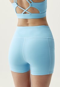 Modré sportovní šortky s hladkou texturou a přiléhavým designem. Mají vysoký pas a decentní švy.