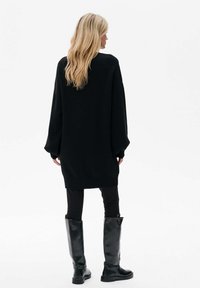 Czarny oversized sweter z długimi rękawami, wykonany z miękkiego materiału, zestawiony z czarnymi legginsami i błyszczącymi czarnymi botkami do kolan.