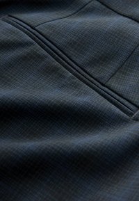 Ciemna tkanina o subtelnym wzorze kratki, cechująca się gładką fakturą i delikatnym połyskiem. Zawiera widoczny detal szwu.