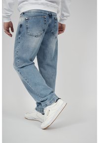 Ljusblå denimjeans med lös passform, med bakfickor och kopparfärgade nitar, i kombination med vita sneakers.