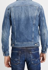 Jeansjacka i medelblått med en strukturerad passform, med klassisk krage, knappstängning och kontrasterande sömmar på bakfickorna.