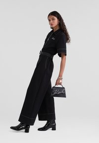 Ensemble noir en deux pièces avec une chemise à manches courtes et un pantalon à jambes larges. Présente des coutures blanches contrastantes. Accessoirisé avec un sac noir.