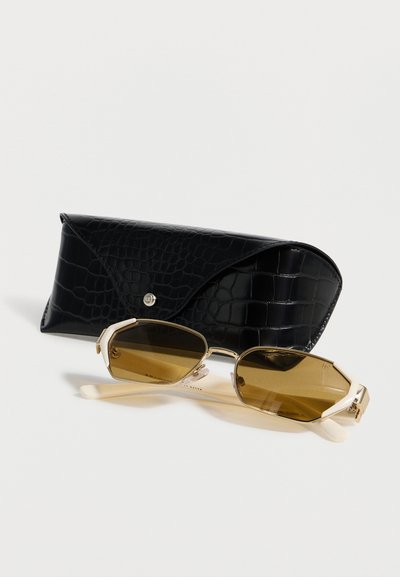 Ορθογώνια γυαλιά ηλίου με χρυσαφένιο πλαίσιο και καφετί φακούς, τοποθετημένα μπροστά από μια μαύρη υφασμάτινη σκληρή θήκη με κούμπωμα.