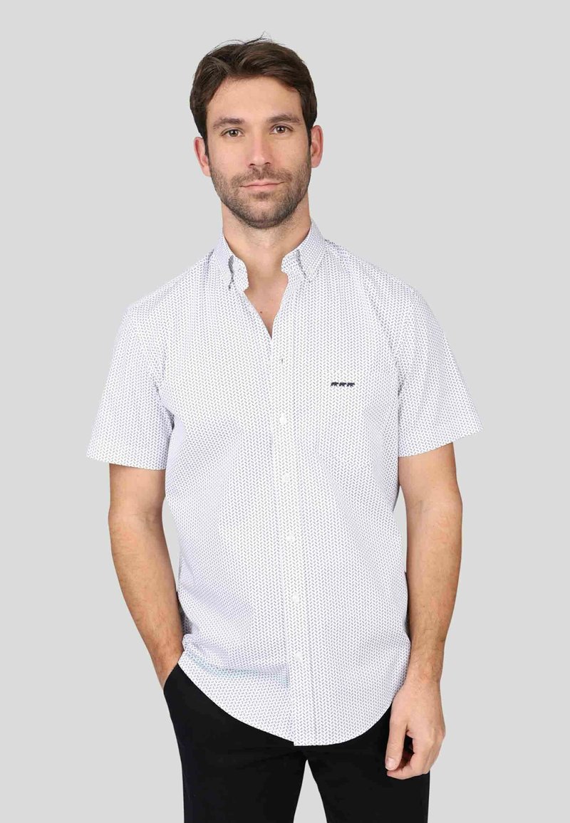 Chemise à manches courtes boutonnée en blanc avec un petit motif géométrique bleu, un col classique et une poche poitrine. Tissu en coton.