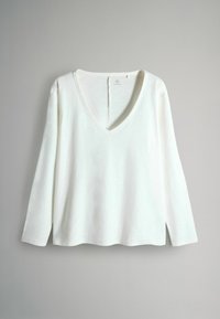 Hvid langærmet V-hals top med en afslappet pasform. Blød tekstur, rundet kant og sideslidser for åndbarhed. Minimalistisk design.