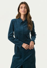 Blaues Cord-Kleid mit langen Ärmeln, Kragen, vertikaler Struktur, vorderer Knopfleiste und seitlichem Schlitz.