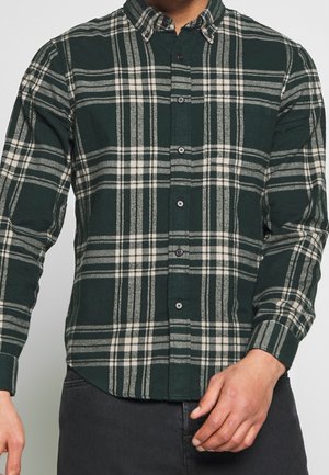 Camisa de cuadros verde y gris de botones, hecha de franela, con cuello puntiagudo, mangas largas y botones negros a lo largo del frente.